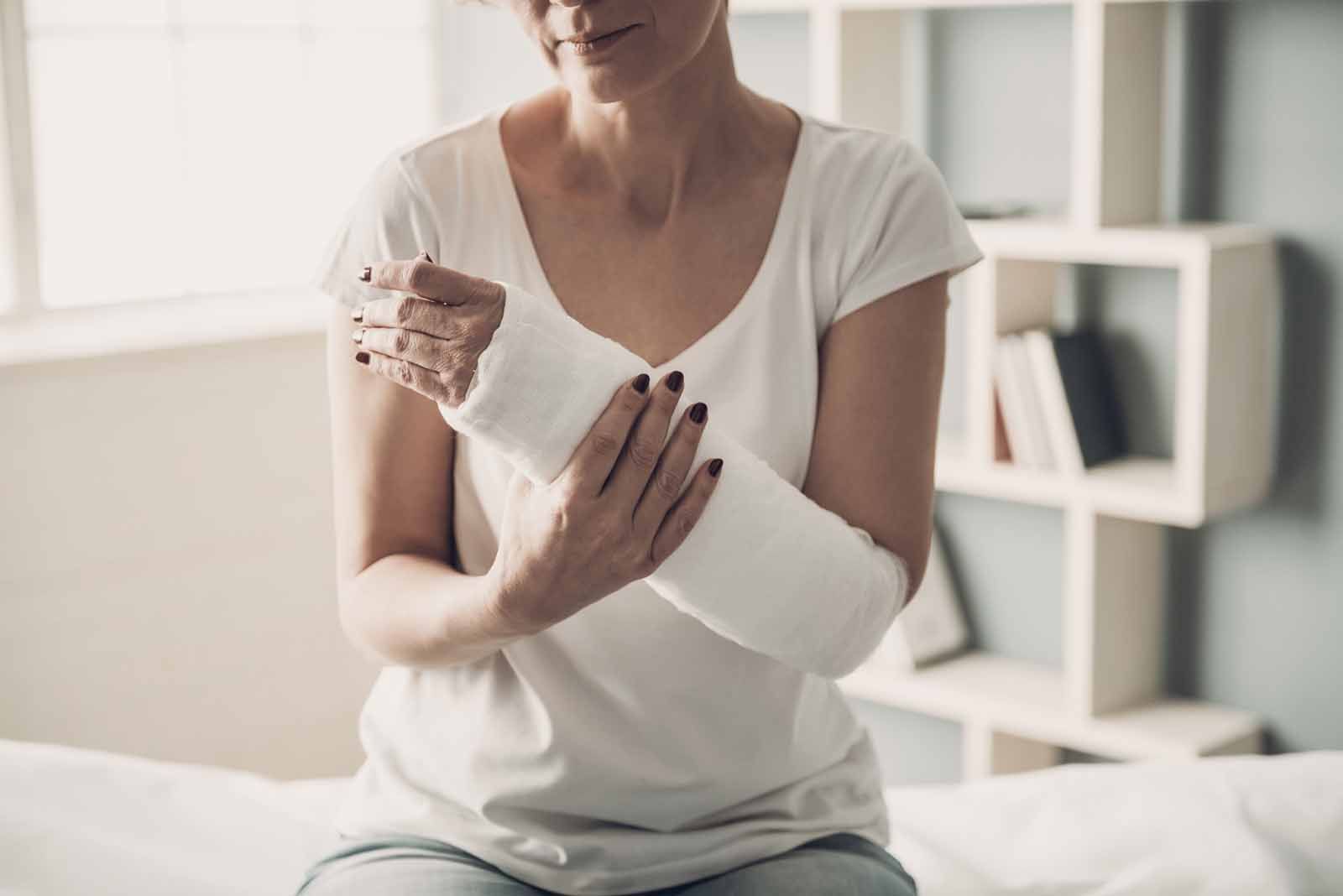 A woman with a cast on her arm is sitting on a bed.