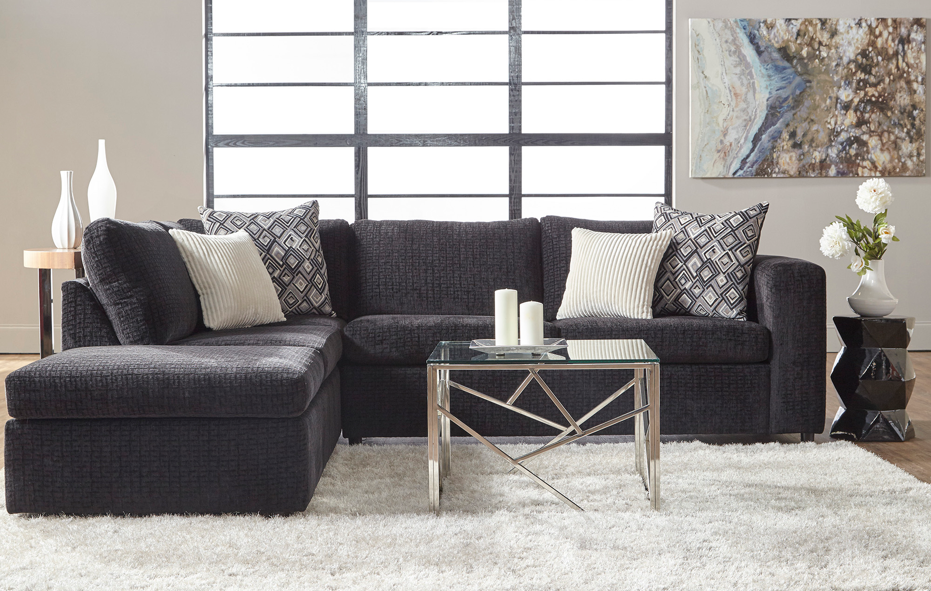 Dark sectional sofa with pillows, glass table, fluffy white rug.