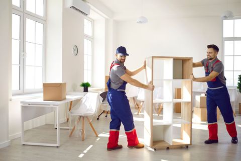 Two men are moving a shelf in a room.