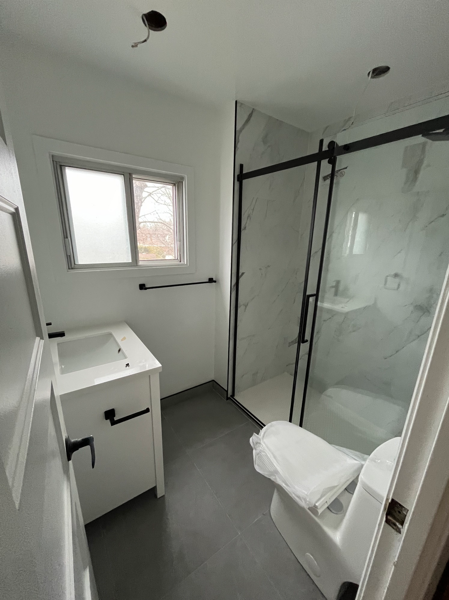 Petite salle de bains moderne avec lavabo, toilettes, fenêtre et cabine de douche en verre.