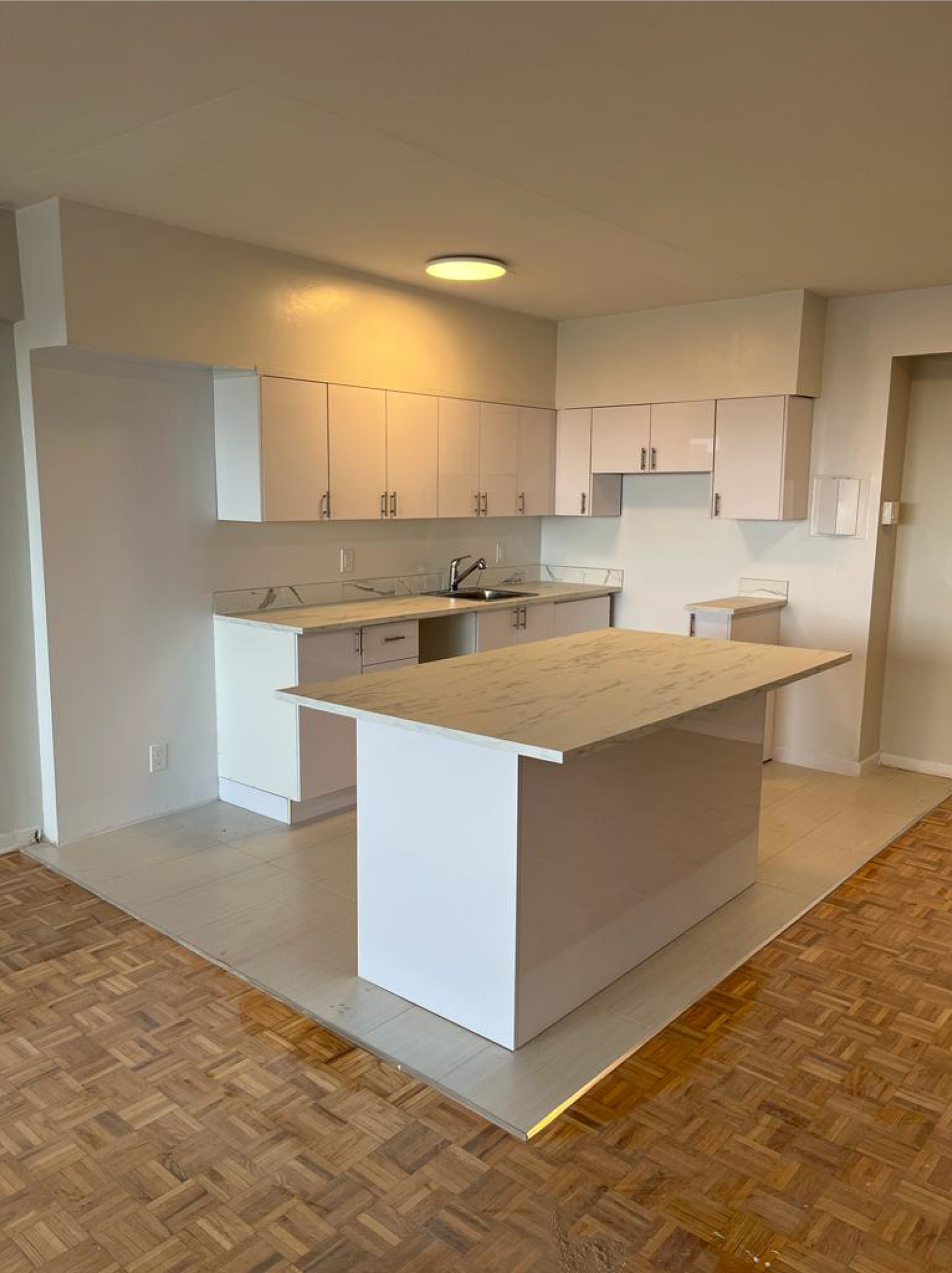 Cuisine vide avec placards blancs, îlot en granit et parquet.