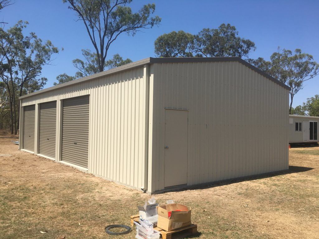 A Large White Metal Building With Three Garage Doors is Sitting in the Middle of a Field  — Shedquarters In Kirwan, QLD