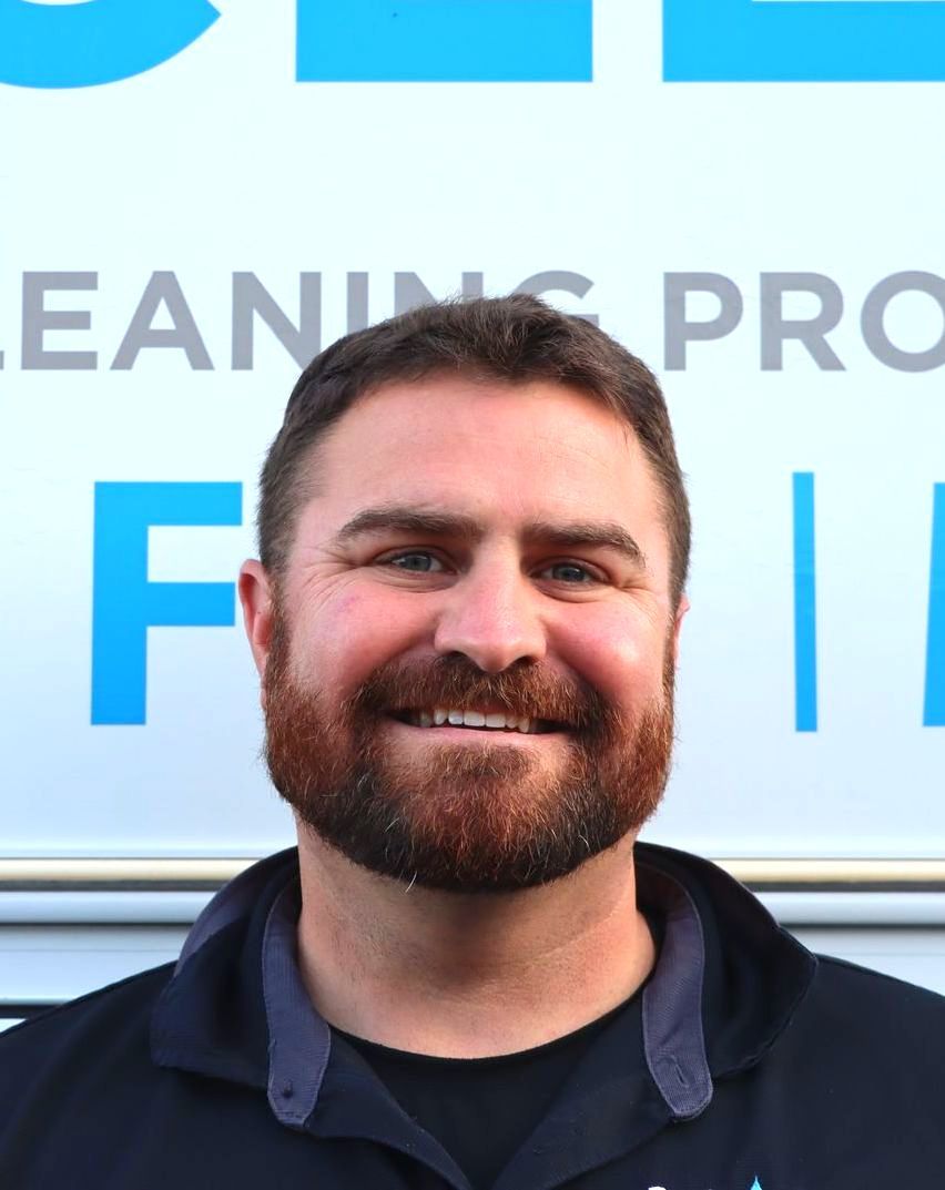 A man with a beard is smiling in front of a sign that says cleaning pro