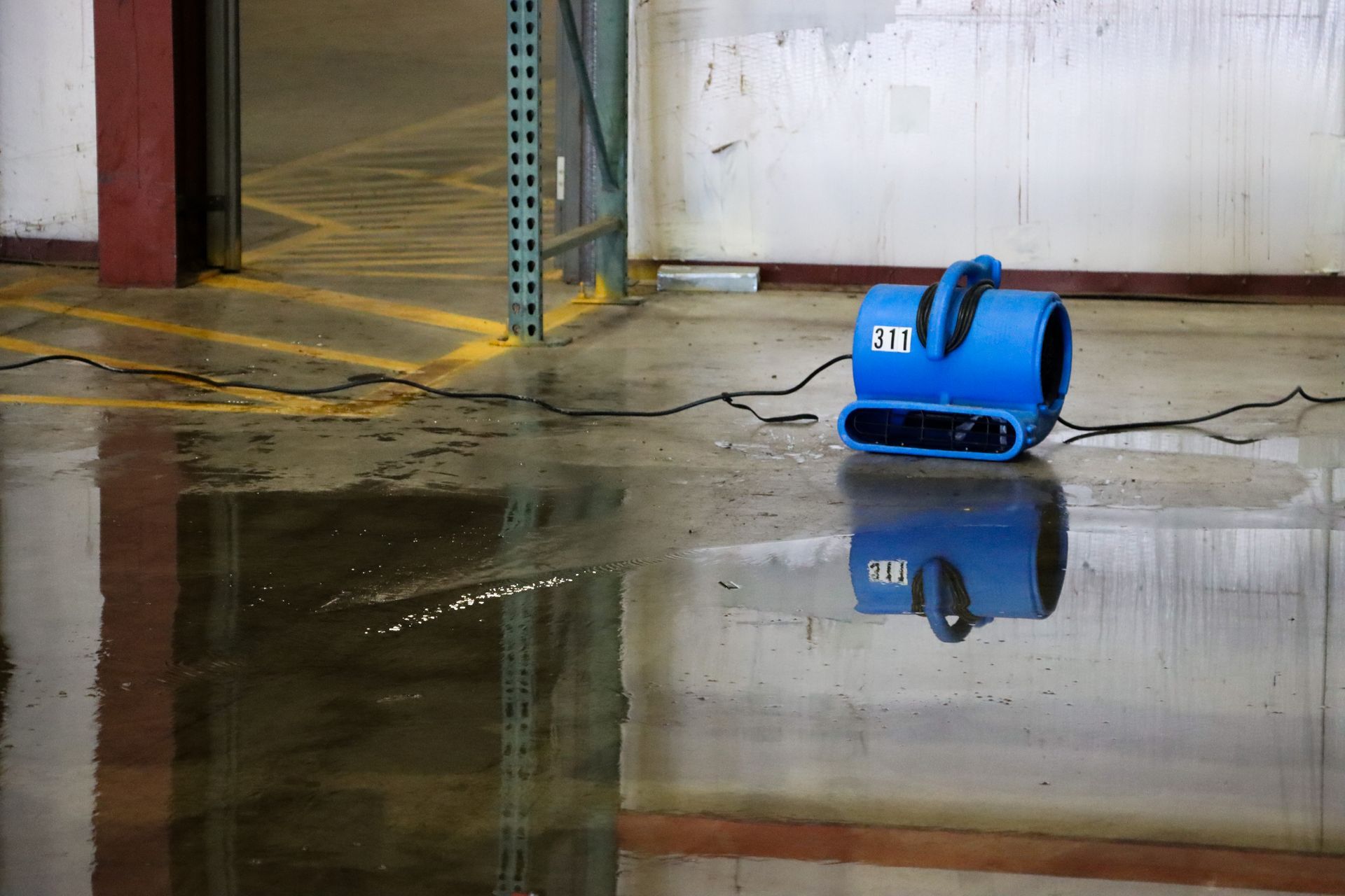 A blue fan is sitting on the floor of a flooded warehouse.