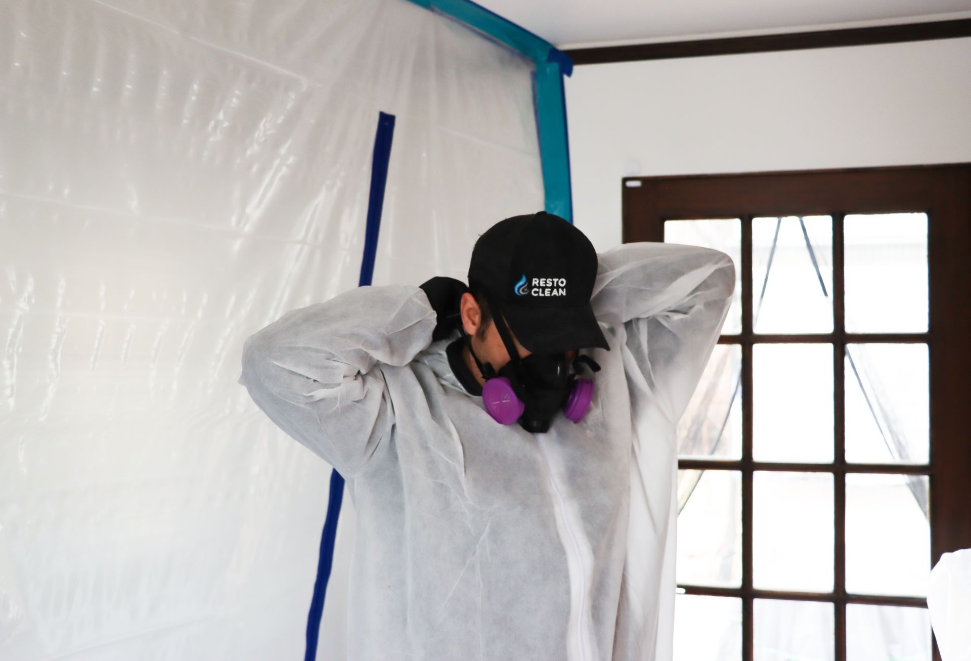 A man wearing a hat and a protective suit is standing in a room.