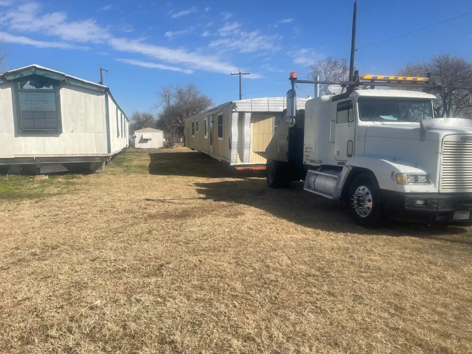 A white semi truck is carrying a trailer in a dirt field.