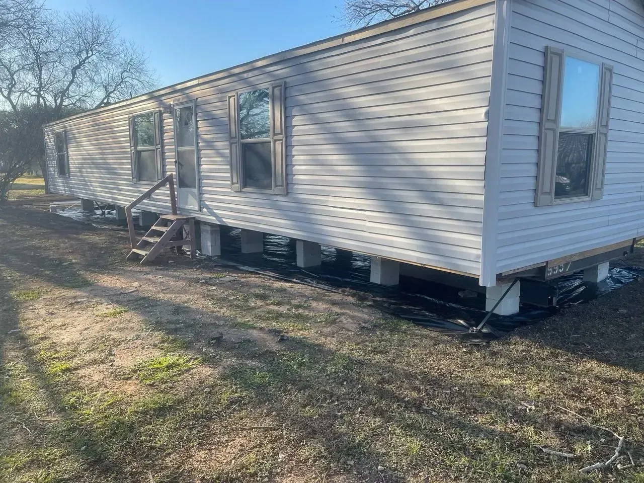 A white mobile home is sitting on top of a dirt field.