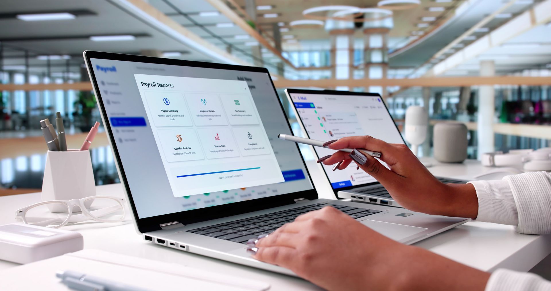 A person using a stylus to navigate payroll software on a laptop in a brightly lit, modern office setting.