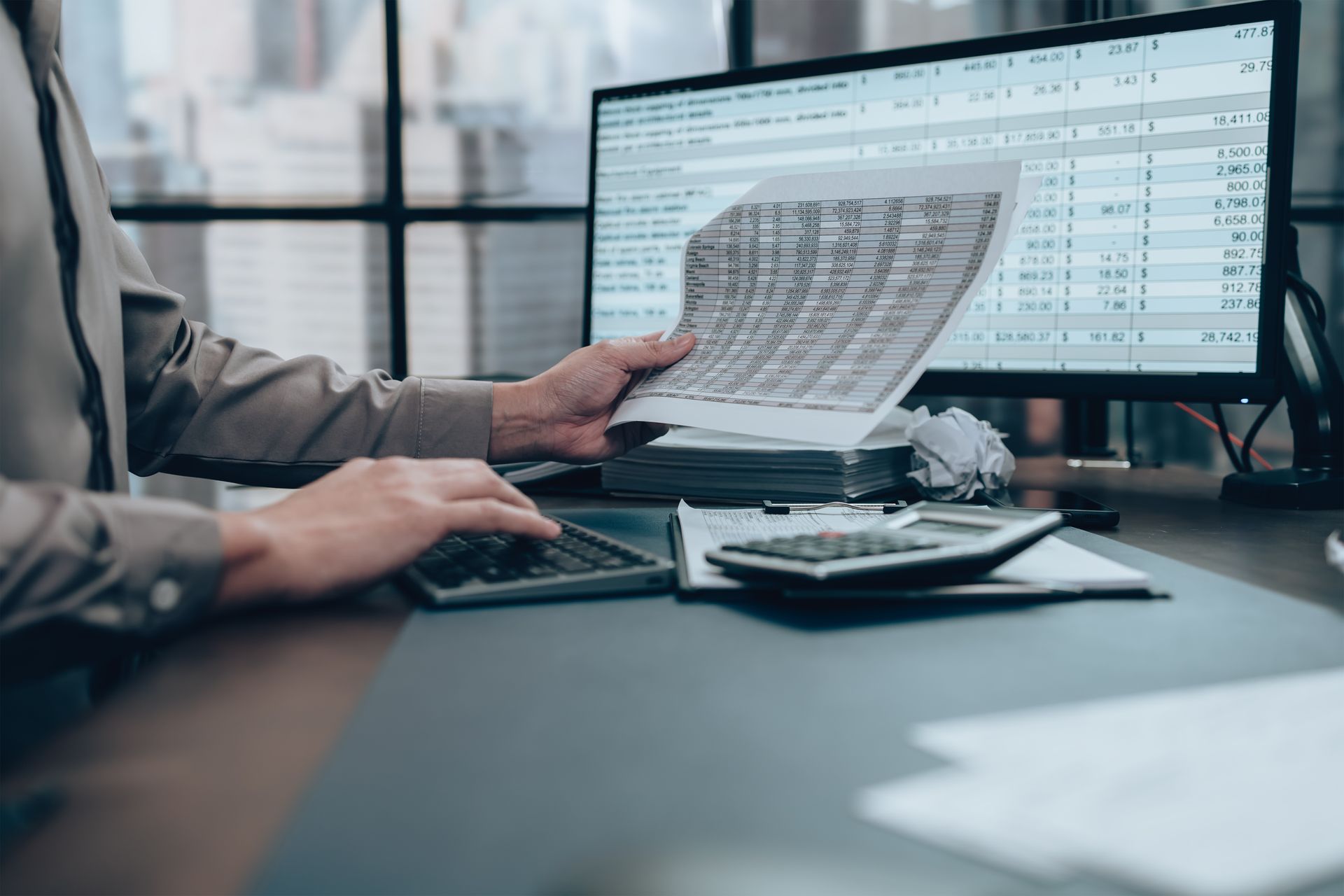 An auditor working at his desk, using a calculator and computer while reviewing statements. An auditor working at his desk, using a calculator and computer while reviewing statements.