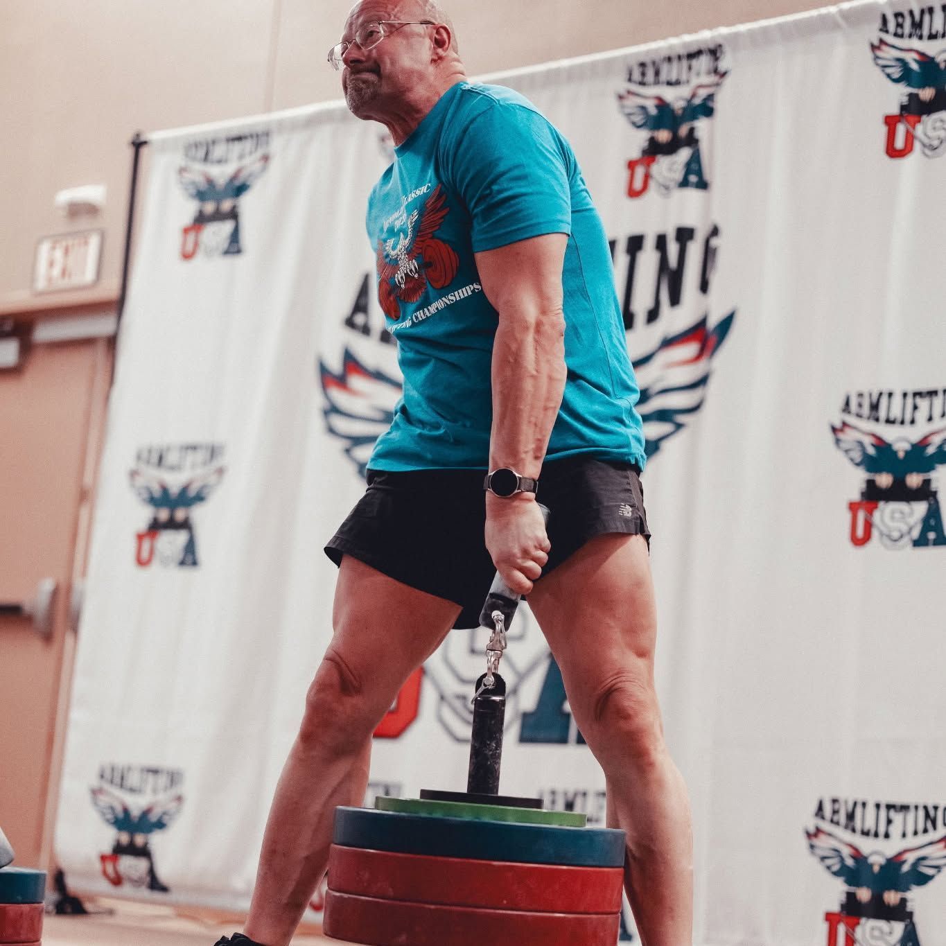 Person lifting weights indoors, standing on stacked plates at a competition event.