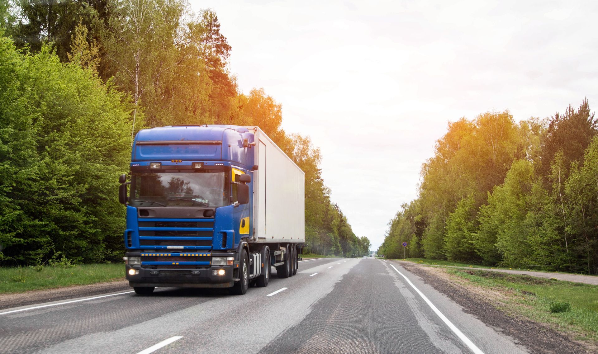 Blue semi-truck driving on a tree-lined road at sunset. Blue semi-truck driving on a tree-lined road at sunset.