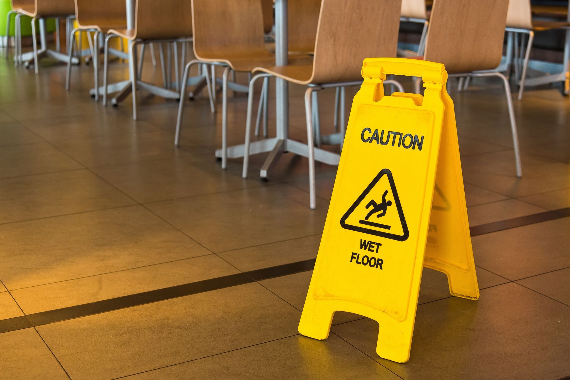 Yellow wet floor caution sign on a tiled floor in a cafeteria or dining area. Yellow wet floor caution sign on a tiled floor in a cafeteria or dining area.