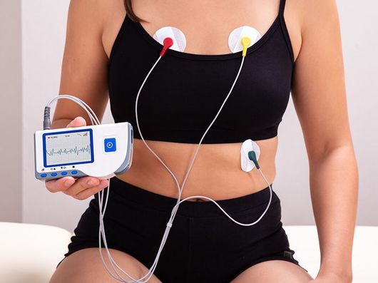 Una donna è seduta su un letto con un cardiofrequenzimetro attaccato al petto.