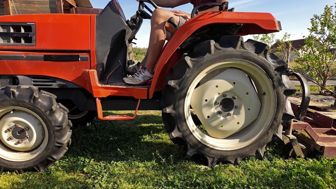 Orange tractor parked on grass, side view with large rear wheel and cab. Orange tractor parked on grass, side view with large rear wheel and cab.