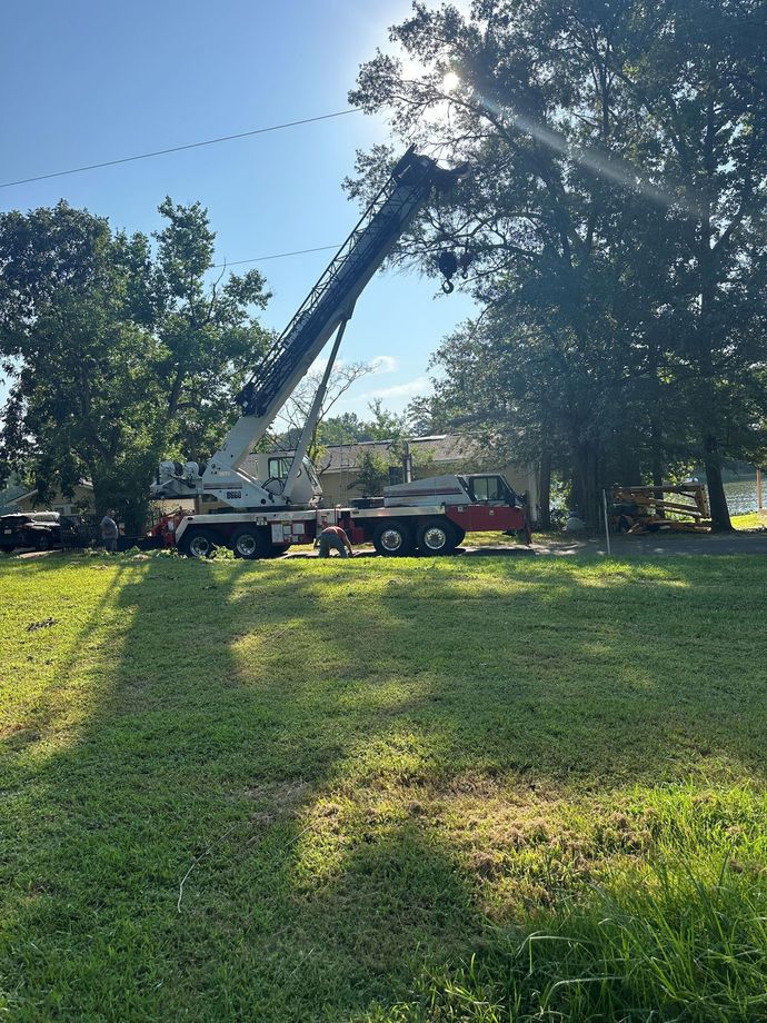 Crane truck with raised boom parked on a grassy lawn beside trees in bright sunlight Crane truck with raised boom parked on a grassy lawn beside trees in bright sunlight