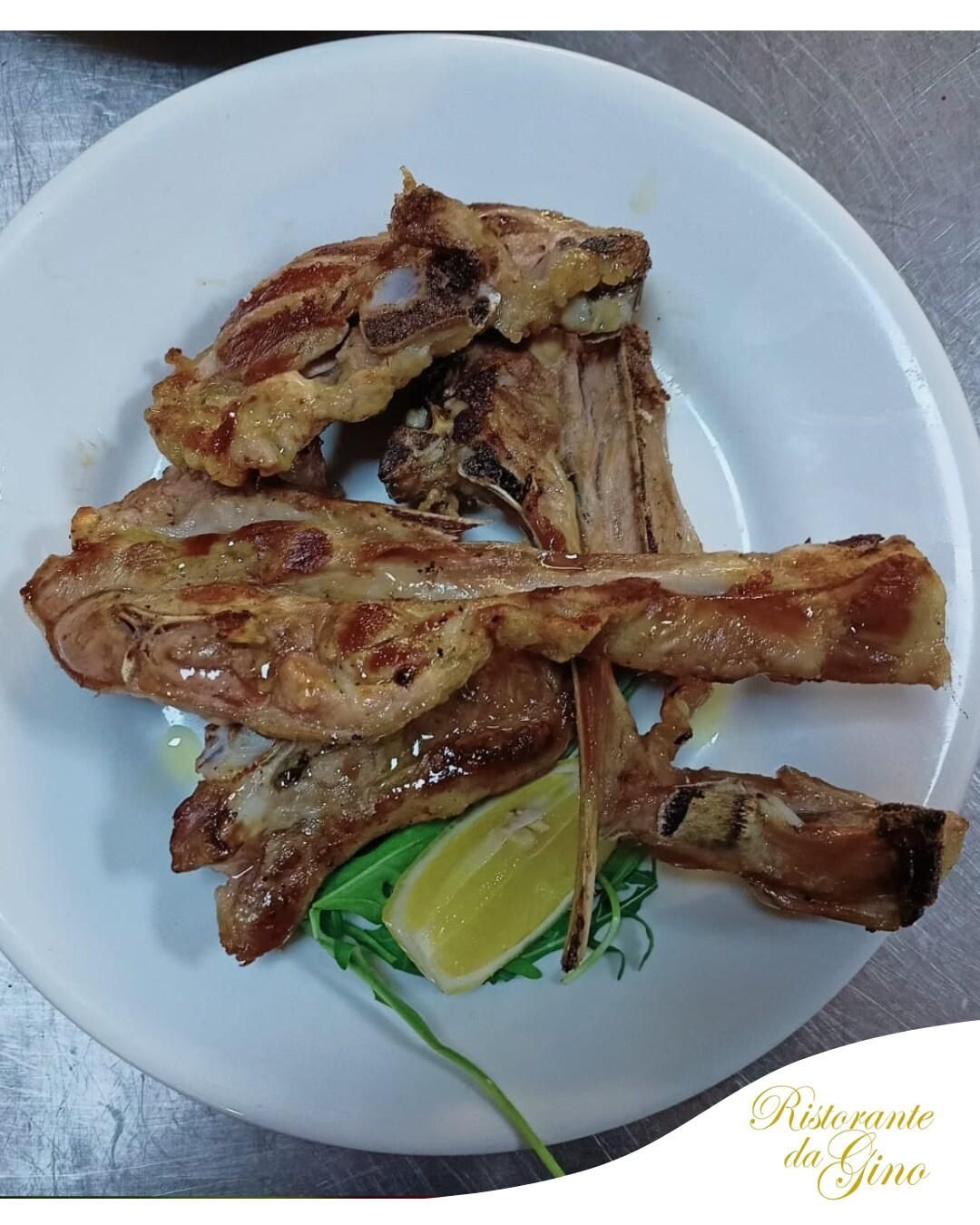 Piatto di pezzi di carne grigliata con uno spicchio di lime ed erbe aromatiche su un piatto bianco.