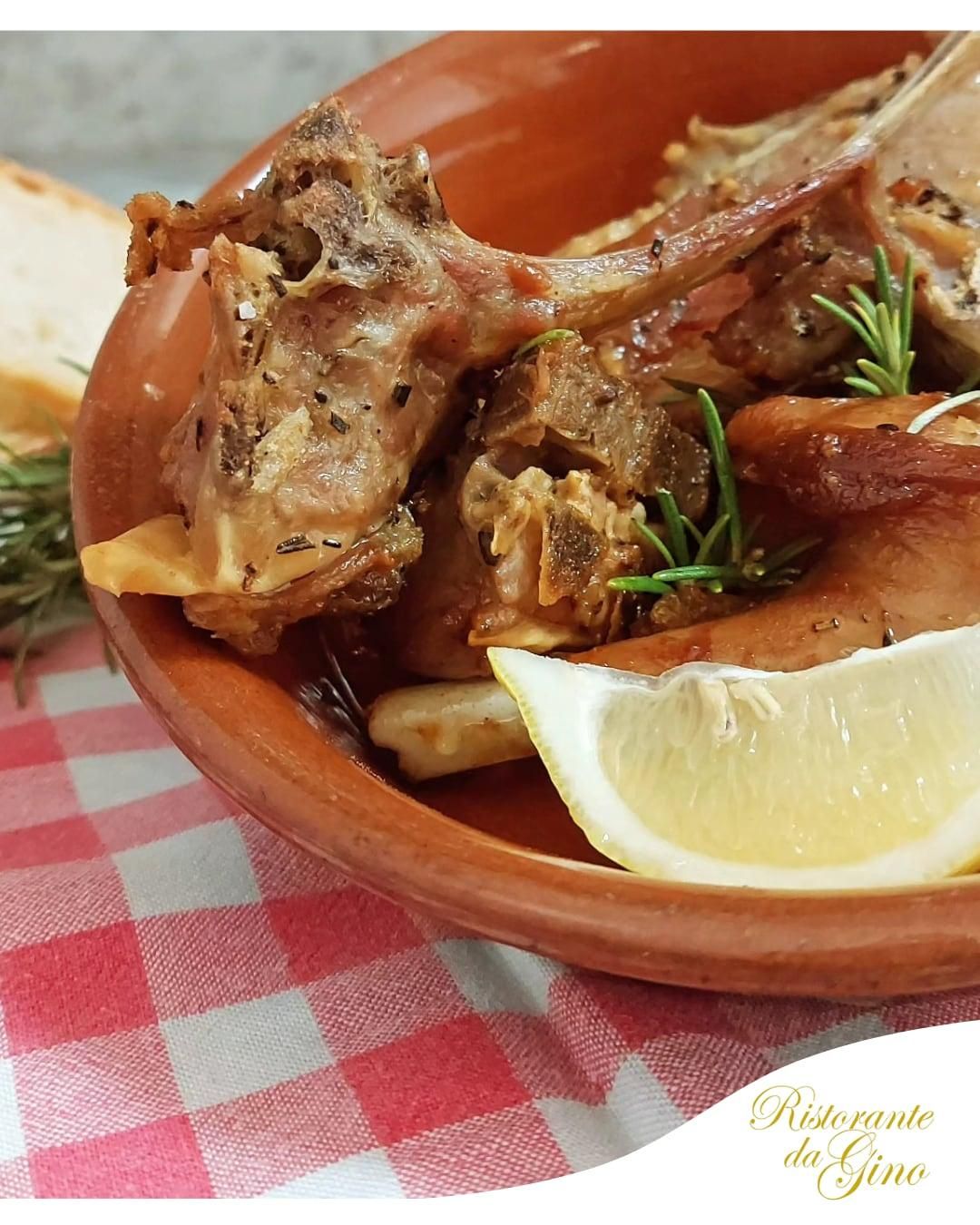 Carne arrosto su un piatto marrone con spicchi di limone ed erbe aromatiche su una tovaglia a quadri rossi.
