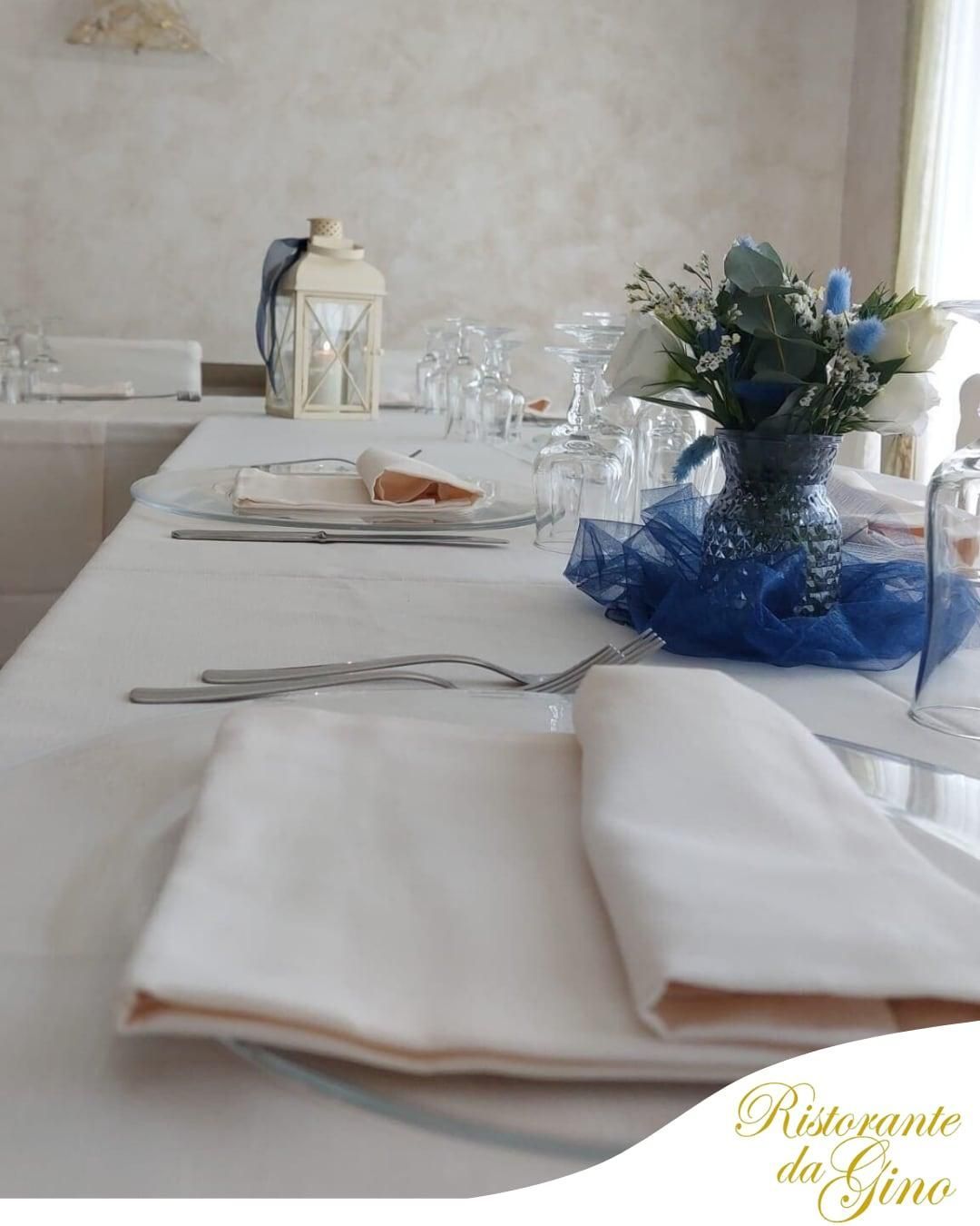 Elegante tavolo da pranzo con tovaglie e bicchieri bianchi, decorato con un centrotavola floreale blu.