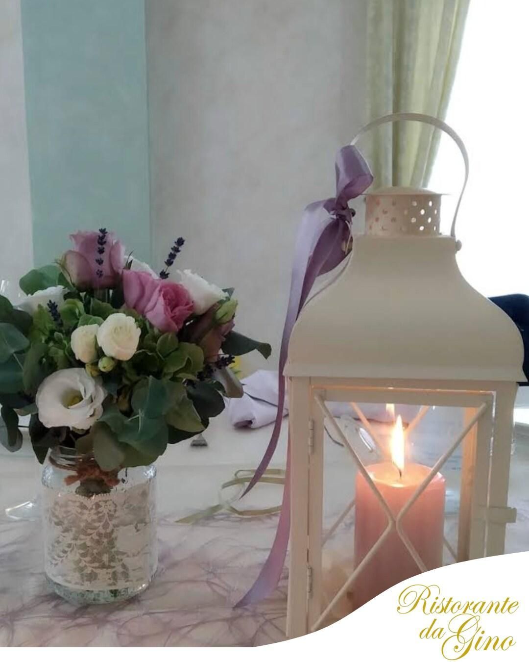 Un mazzo di fiori in un vaso di vetro accanto a una lanterna bianca accesa con una candela, su un tavolo di marmo.