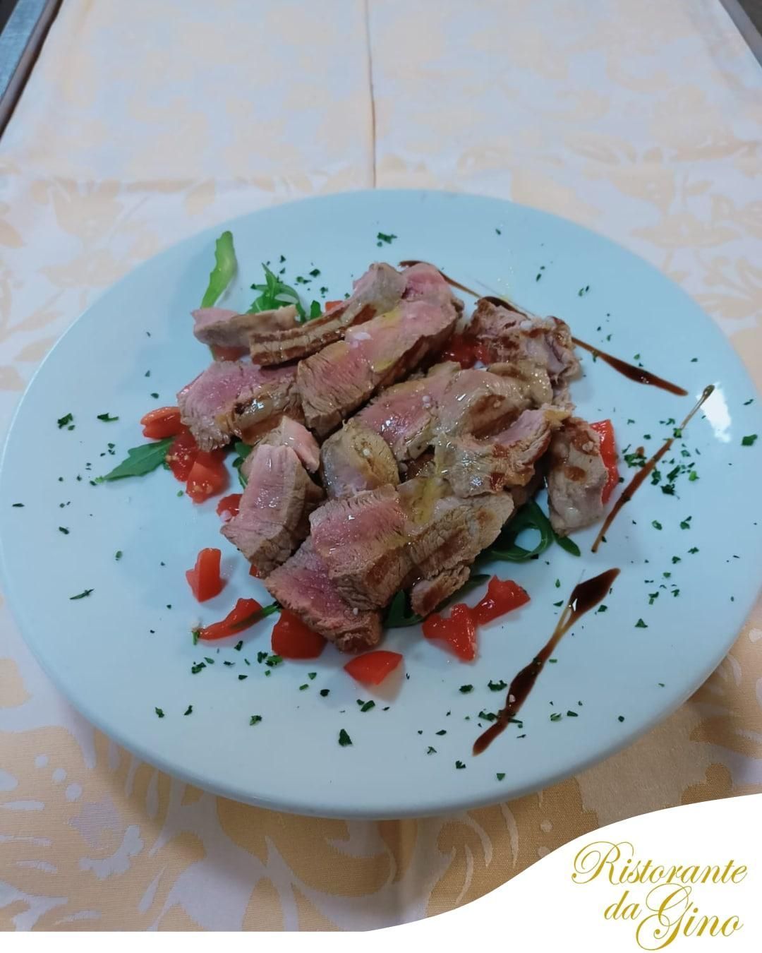 Fettine di bistecca grigliata su un piatto bianco, guarnite con erbe aromatiche e peperoni rossi su una tovaglia.