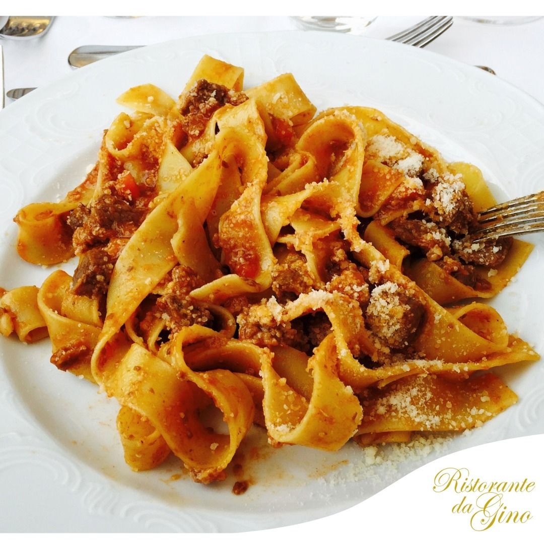 Piatto di pappardelle al ragù e formaggio grattugiato su un piatto bianco.
