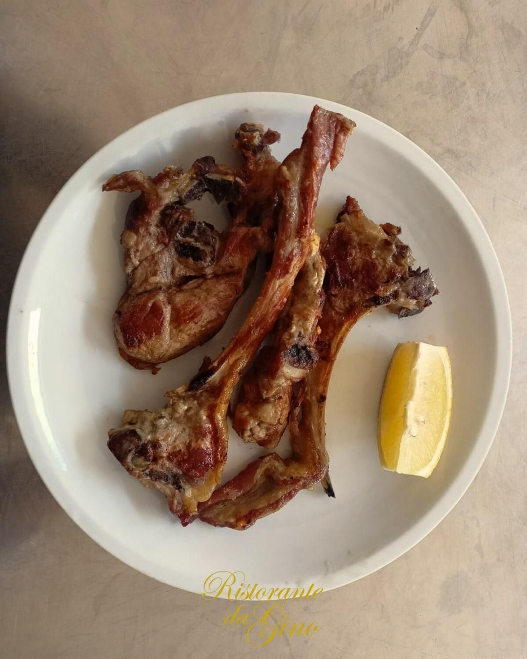 Piatto con pezzi di carne grigliata e uno spicchio di limone su una superficie beige.