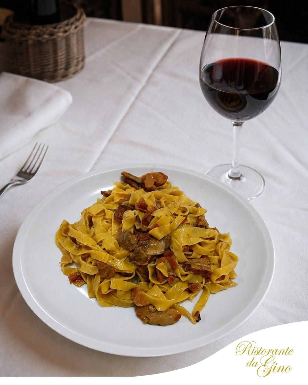 Pasta al ragù su un piatto bianco accanto a un bicchiere di vino rosso su un tavolo