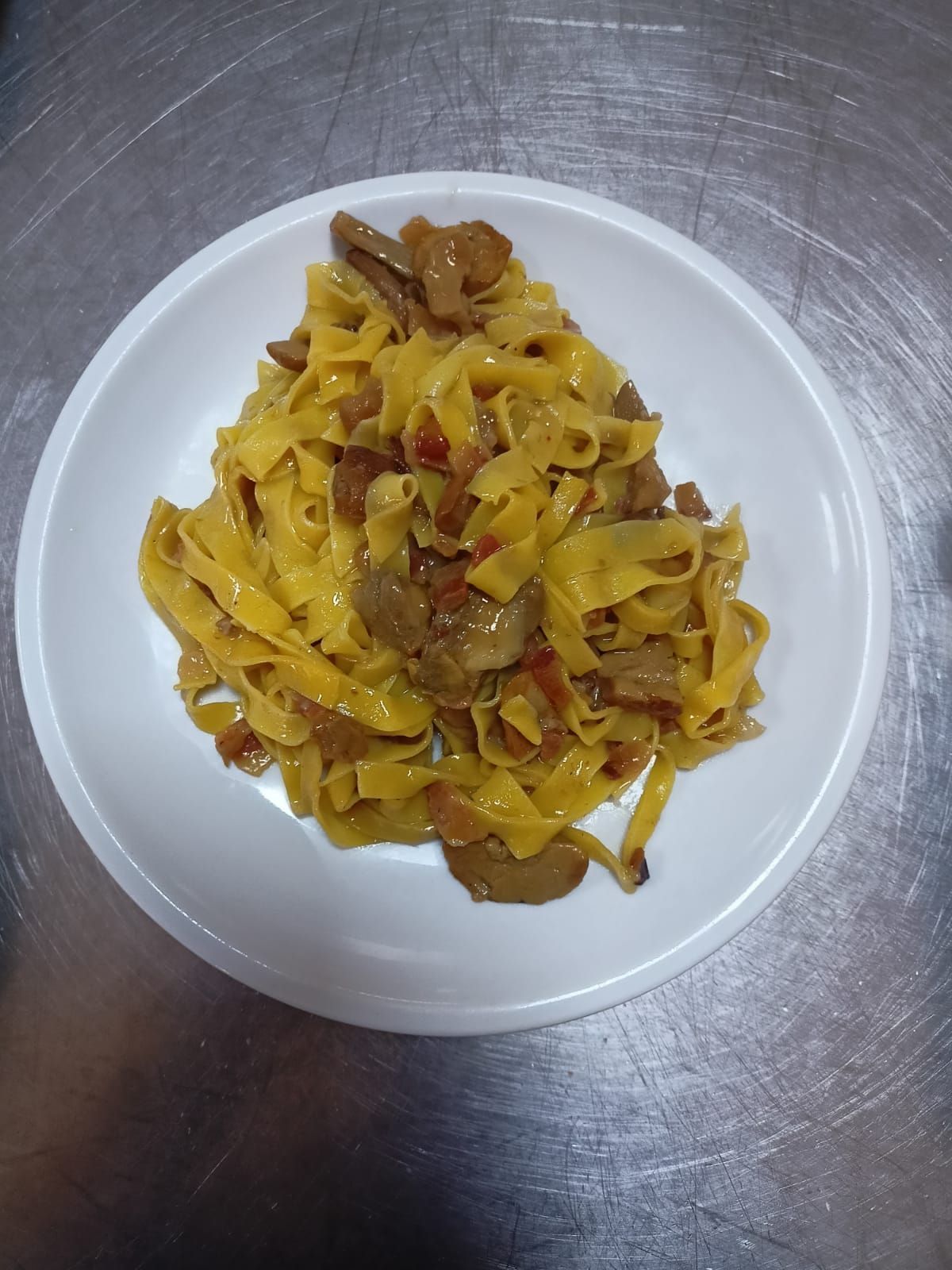 Piatto di pasta gialla al ragù su un piatto bianco, su un piano di lavoro in metallo.