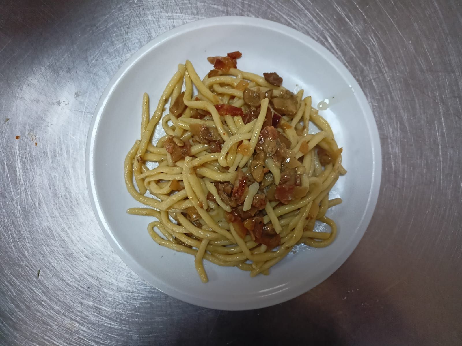 Una ciotola di pasta con verdure su un piano di lavoro in metallo.