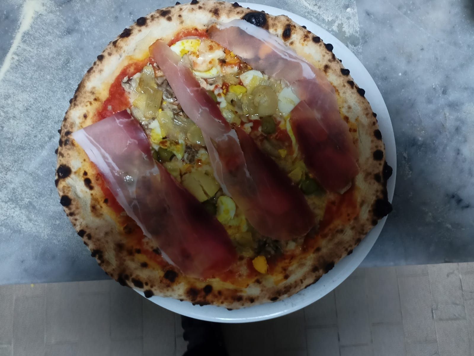 Pizza con salame piccante e verdure su un piatto bianco con carta da forno sotto