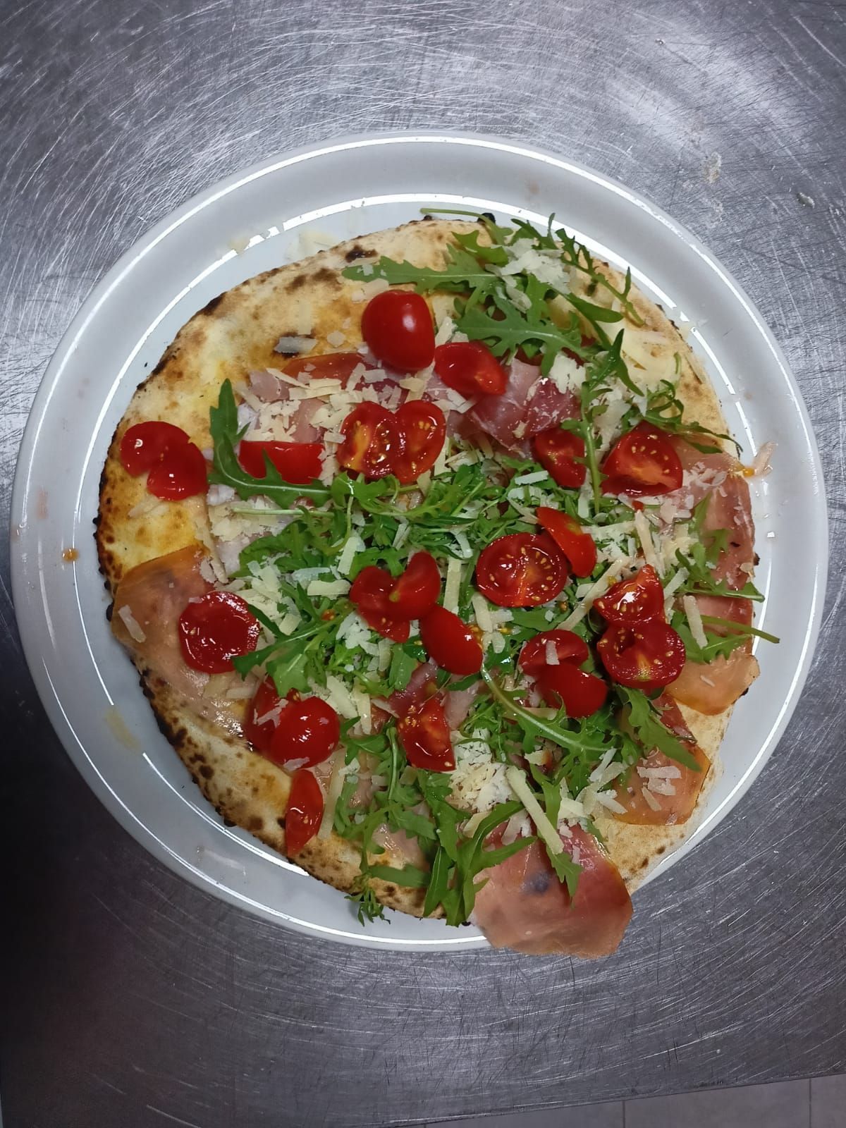 Pizza piccola su un vassoio di metallo, guarnita con pomodorini e rucola.