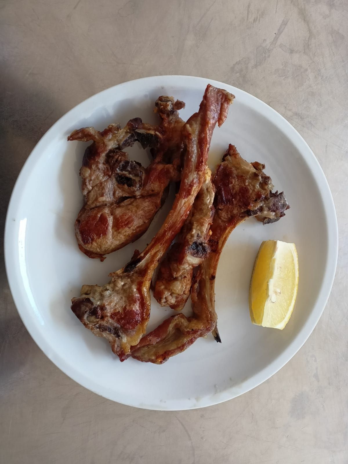 Piatto con pezzi di carne grigliata e uno spicchio di limone su un piano di lavoro chiaro.