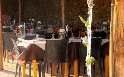 Sala da pranzo rustica del ristorante con tavoli apparecchiati, sedie in vimini e un centrotavola floreale bianco.
