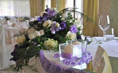 Centrotavola floreale viola e bianco con candele su un tavolo da pranzo decorato.