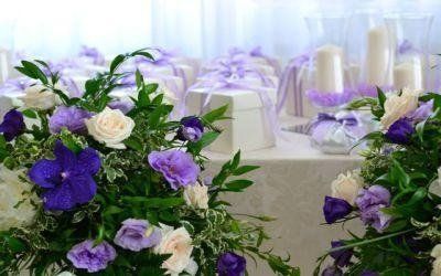 Composizioni floreali viola e bianche decorano un tavolo nuziale illuminato da luci soffuse.