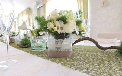 Centrotavola floreale bianco in un vaso di vetro su un runner da tavola verde a fantasia, su un tavolo decorato per un evento.
