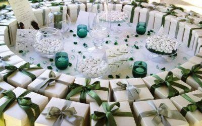 Scatole regalo bianche con nastri verdi disposte in cerchio attorno a un tavolo decorato con dettagli verdi e candele.