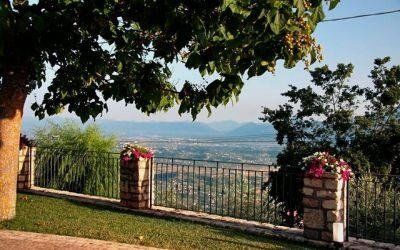 Giardino ombreggiato con recinzione, vasi di fiori e vista panoramica sulla città e sulle montagne in lontananza.