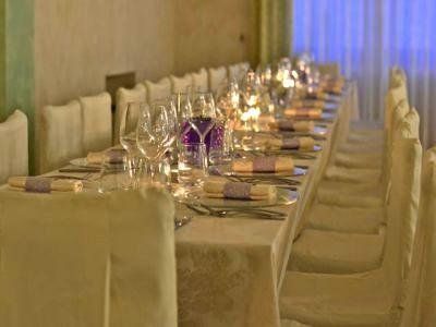 Elegante tavolo da pranzo apparecchiato con calici da vino, candele e sedie beige in una stanza illuminata da luci soffuse.