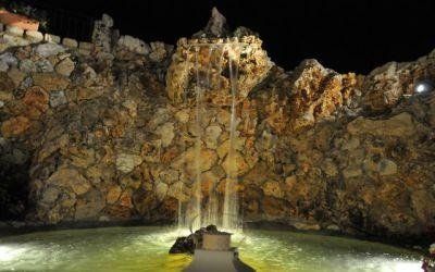Parete rocciosa di una grotta con una piccola cascata o un ruscello che sfocia in una pozza illuminata di notte.
