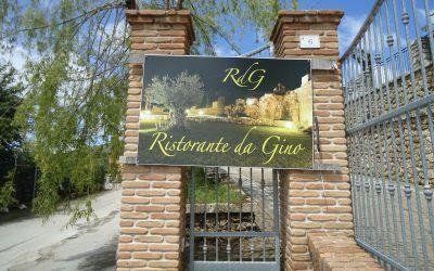 Cartello d'ingresso del Ristorante da Gino su un pilastro di mattoni, con un vialetto d'accesso chiuso da un cancello e il cielo azzurro sullo sfondo.
