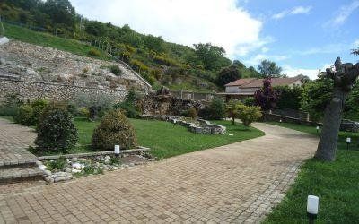 Sentiero lastricato in pietra nel giardino, accanto a terrazze verdi e fiorite sotto un cielo azzurro.