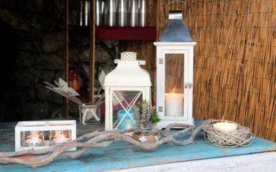 Lanterna bianca decorativa e candele su un tavolo rustico con legni di mare e un portacandele in vimini.
