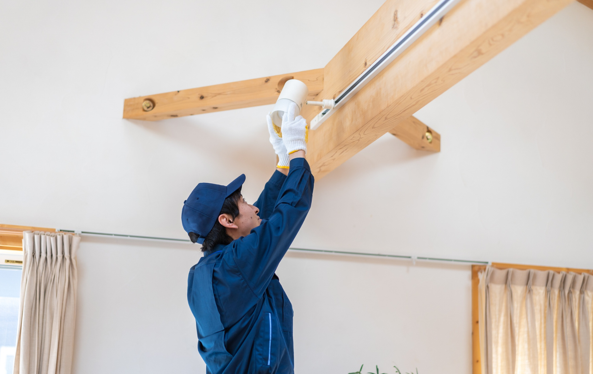 Worker in blue coveralls installing a wooden ceiling beam indoors with a power tool