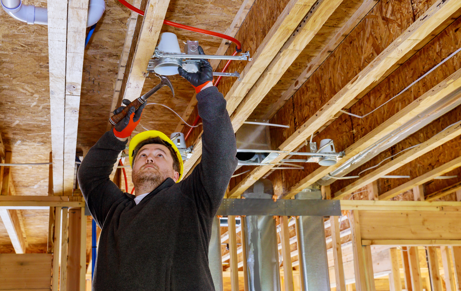 Construction worker in hard hat installing wiring in an unfinished wooden ceiling