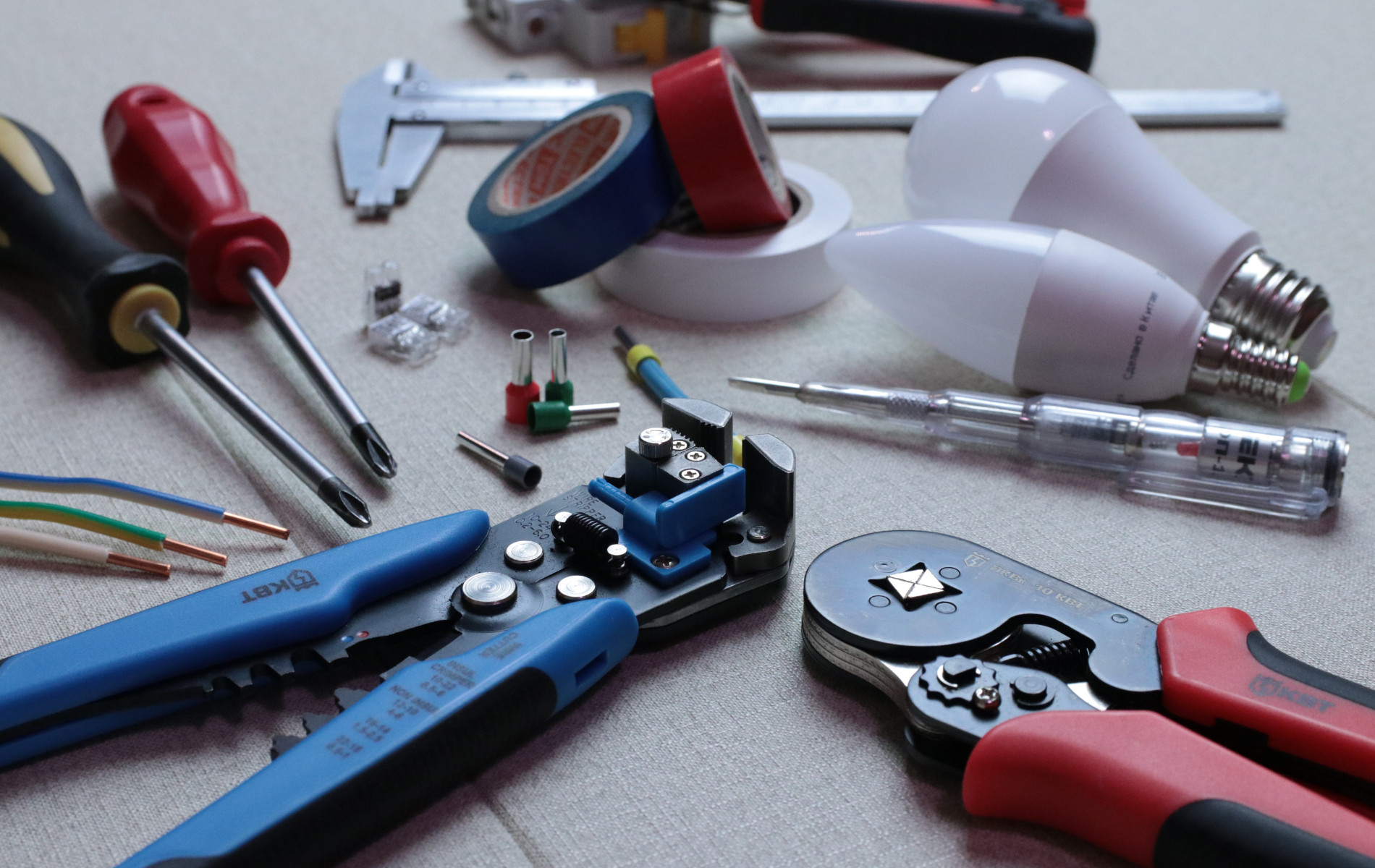 Assorted electrical tools and bulbs on a work surface, including pliers, screwdrivers, tape, and wires