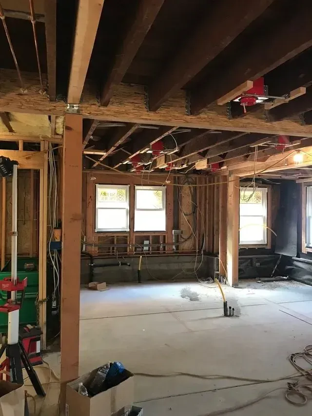 Interior of a gutted room under renovation, with exposed beams, wiring, and unfinished walls.