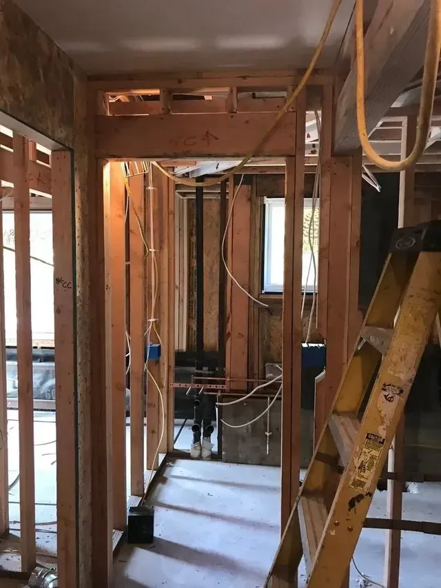 Interior under construction with exposed wooden framing, a ladder, and unfinished walls.