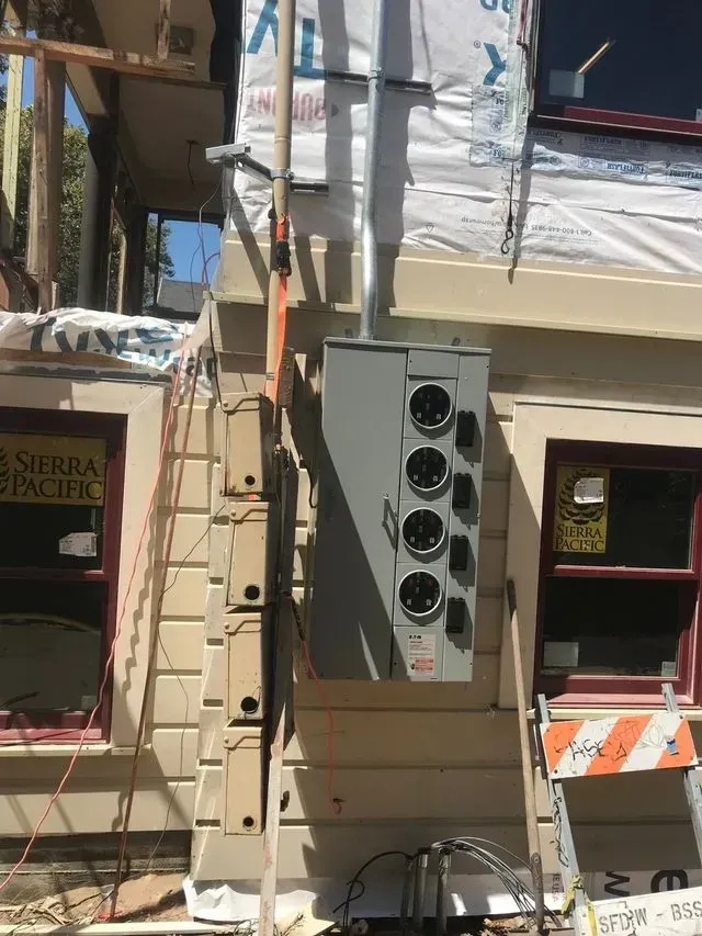 Wall-mounted air-conditioning unit on a beige building exterior with nearby windows and construction scaffolding.