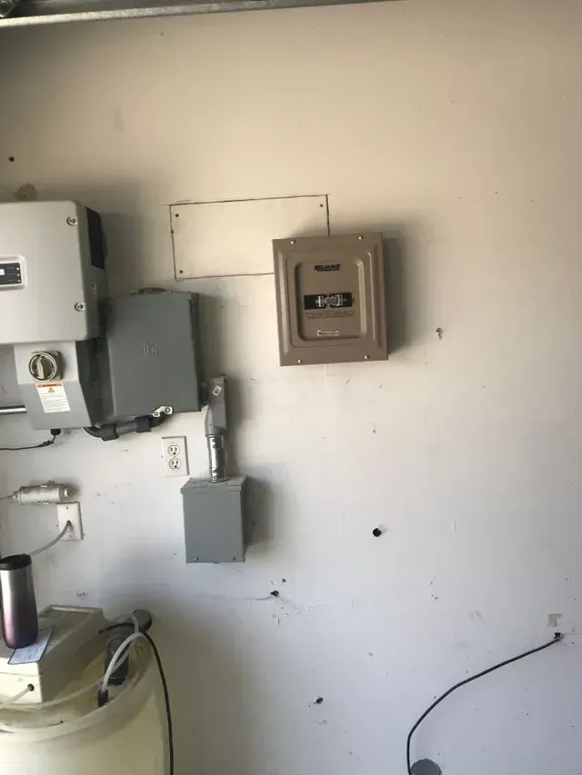 Electrical service boxes and meters mounted on a plain white wall in a utility area.